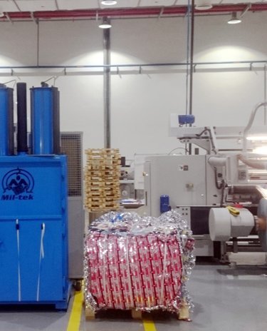 man with white hat standing in printing production next to blue waste baler and a compacted bale